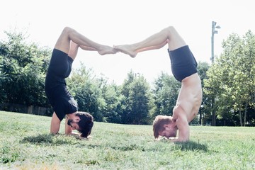 Two men poised upside down in yoga position in park