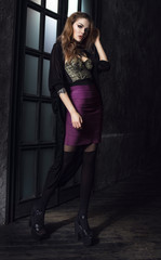 Sexy young woman in violet skirt standing in vintage dark interior