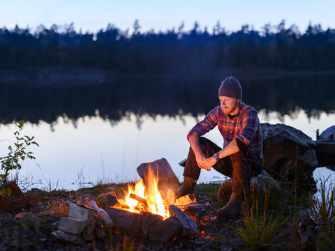 Man sitting at bonfire near lake