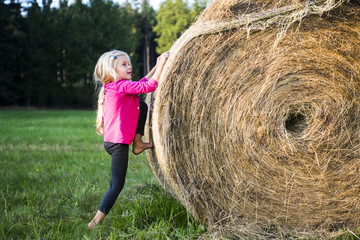 Naklejka na ściany i meble Child blond Girl by straw hay bale in field, meadow, playing, children summer activities