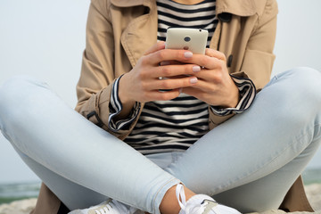 Girl holding smart phone with two hands sitting on the beach san