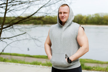 Naklejka na ściany i meble Workout man in hood resting by the river outdoor.