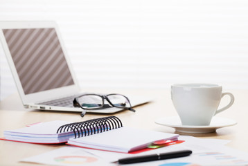 Office workplace with laptop, coffee and reports