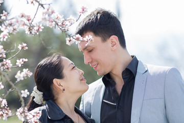 Fototapeta premium Asian girl and european guy among of blossoming almond branches