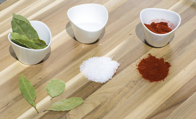 Spices in small dishes on a tray. Salt, red pepper and Bay leaf on a wooden background. 