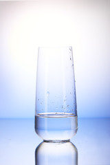 One-third full drinking glass with reflection in drops of water