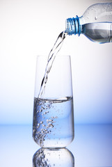 Water pouring from plastic bottle in half-filled drinking glass