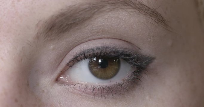 Big close up of a woman's brown eye looking at the camera and looking around.  Low contrast look, recorded in 4K at 60fps.