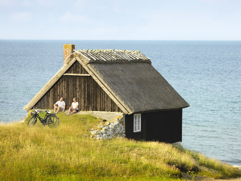 Couple sitting near wooden house at sea
