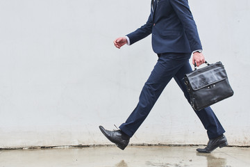 A man in a suit with a briefcase in hand comes against the backdrop of a white wall