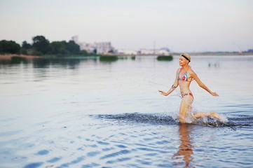 Girl runs into water in swimsuit. Beauty Model Girl Splashing Water with her legs. Beautiful Woman in Water