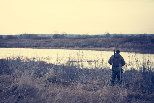 Hunter man standing at river bank in expectation of successful hunting during misty sunrise in rural field and watching on beautiful sunrise  with copy space