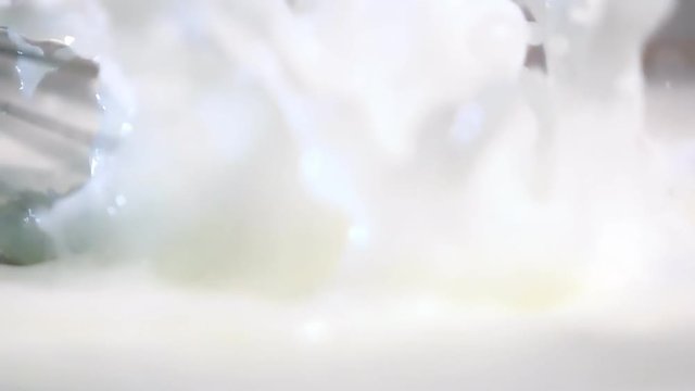 High-speed shot of whisking absolutely white milk with digital blender. Large liquid splashes. Slow motion shooting on Sony rx 10 ii.