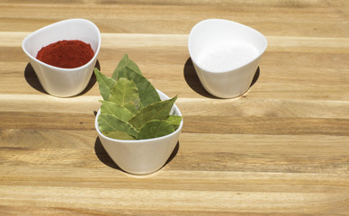 Spices in small dishes on a tray. Salt, red pepper and Bay leaf on a wooden background. 