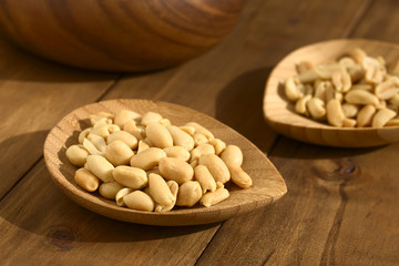 Roasted peeled unsalted peanuts on small bamboo plate, photographed with natural light (Selective Focus, Focus one third into the peanuts on the first plate)