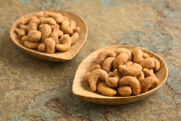 Salted cashew nuts or seeds on small bamboo plates, photographed on slate with natural light (Selective Focus, Focus on the first cashews on the right plate)