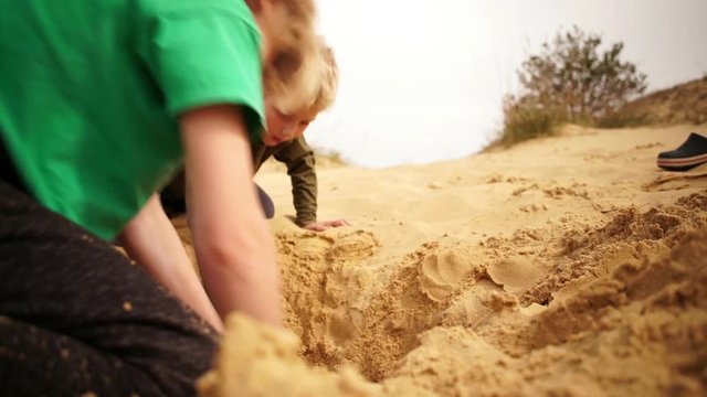 Brothers burrowing hole in sand in Oleshky sands.Ukraine. Slow motion