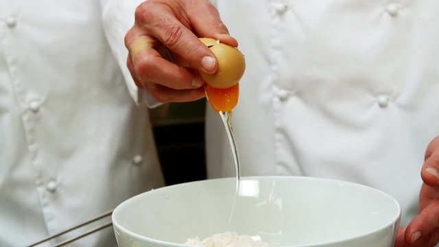 Baker putting an egg in a mixing bowl