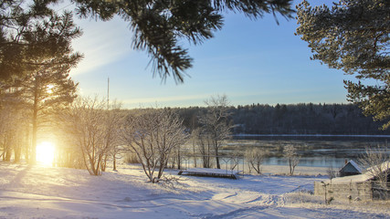 Winter landscape in Russian village during sunset. Snow, river in the background.