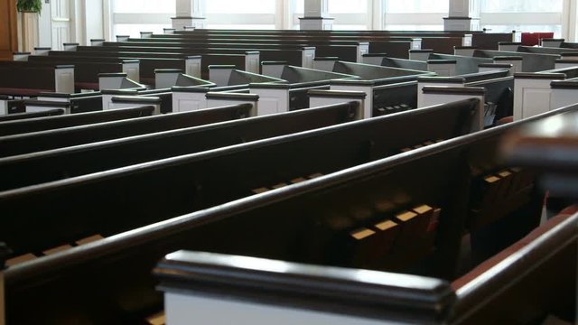 The camera starts behind a pillar and slowly moves (dollies) past wooden pews in a Christian church.