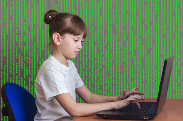 A child plays in a notebook on the background of a green matrix.