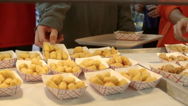Teenage high school student in cafeteria lunch line selects fried foods.