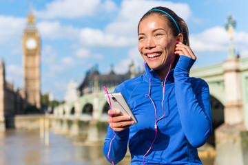 London running lifestyle woman listening to fitness music playlist on smart phone. Female going for run training in urban city street. Runner girl near Big Ben, Westminster Bridge, London, England, UK