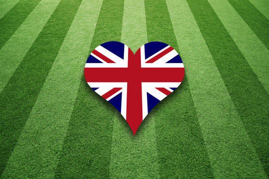 Sunny soccer artificial green grass field with England flag colors heart symbol background.