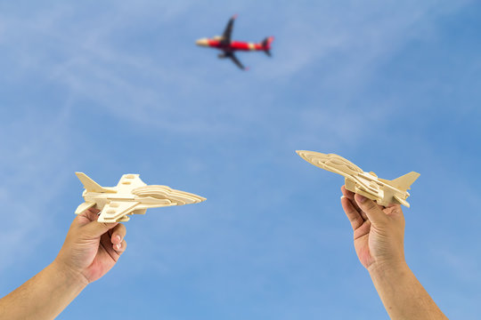 Man's hands holding wooden airplane against blue sky and real airplane