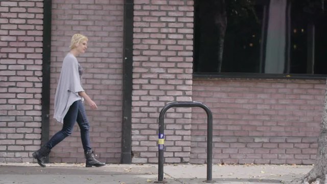 Side view of young woman crossing walking passed brickwork on a street at a crosswalk in Downtown Los Angeles, CA.  Hand-held camera recorded at 135fps.