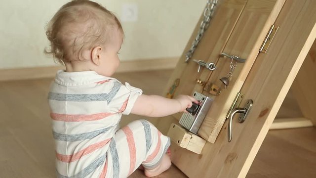 The little boy intently playing with busy board, sitting at the floor