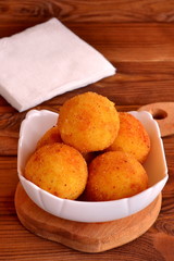 Arancini balls on a plate and on cutting Board. Fried rice cutlets recipe. Brown wooden background 