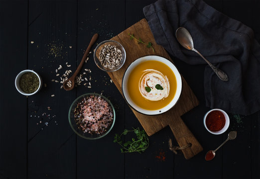 Pumpkin soup with cream, seeds and spices in rustic metal bowl over grunge black background. Top view.