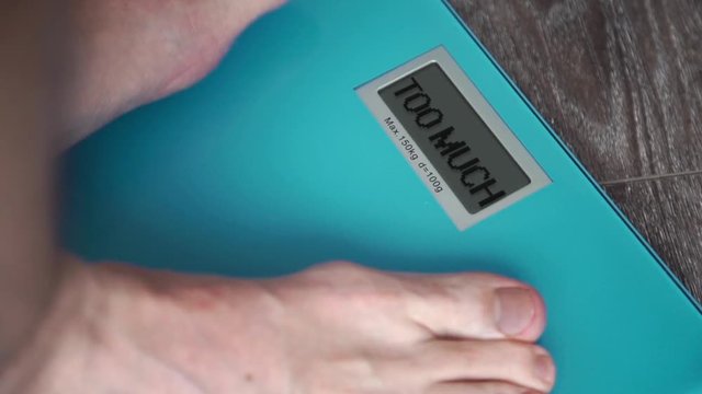 Male legs standing On A Weighing Machineand on display TOO MUCH