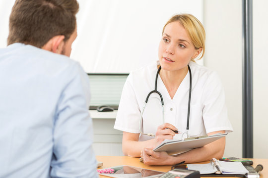 Young attractive woman doctor taking notes while patient speak