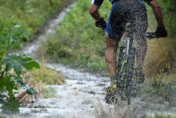 Crédence de cuisine en verre imprimé Vélo Mountain biker driving in rain upstream creek