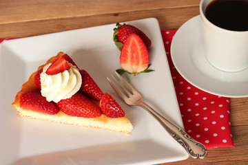 Erdbeeren, ein Stück Erdbeerkuchen mit Sahne auf weißem eckigem Teller mit einer Tasse Kaffee -...