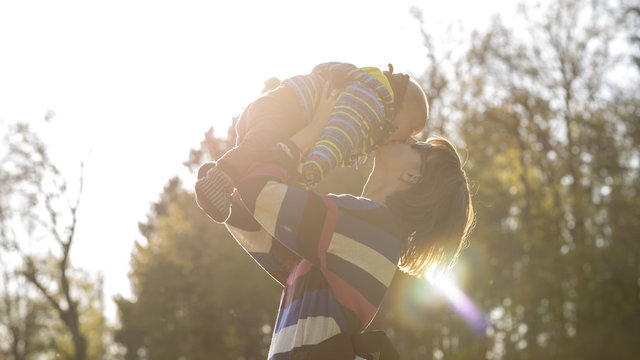 Young Mother Lifting Her Baby In The Air Giving Him A Kiss