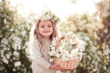 Fototapeta premium Smiling baby girl 3-4 year old holding basket of flowers outdoors. Looking at camera. Childhood.
