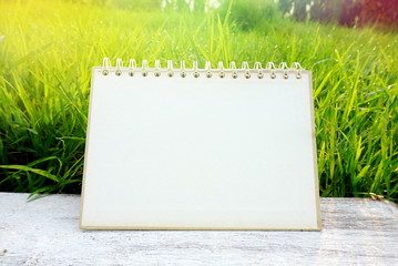blank paper calendar page on white wooden table on nature green field grass with sunlight...