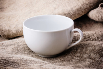 Empty white coffee cup on linen fabric.

