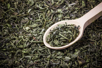 Dry green tea leaves on wooden spoon background.