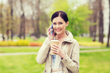 smiling woman with smartphone and coffee in park