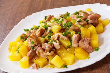 stewed chicken meat with potatoes in a plate on wooden table