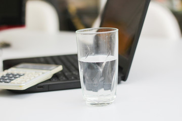 Calculator, laptop and cup of water in a workplace