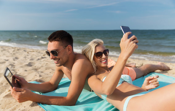 happy couple with modern gadgets lying on beach