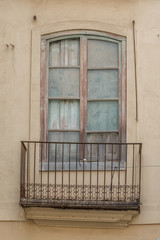 altes Fenster aus verwittertem Holz mit schiefem Balkon und einem verrostetem Geländer