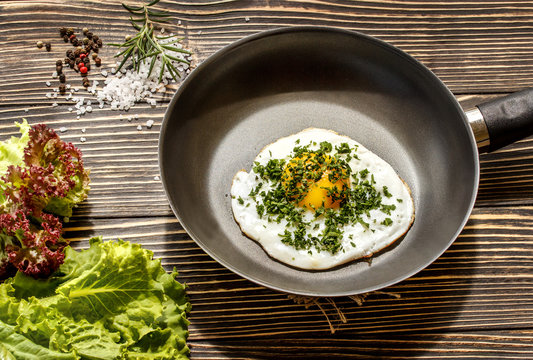 Fried sunny side up eggs on a pan on a brown oak old wooden board