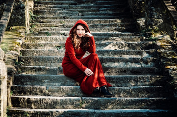 Beautiful woman in red dress sitting on old steps
