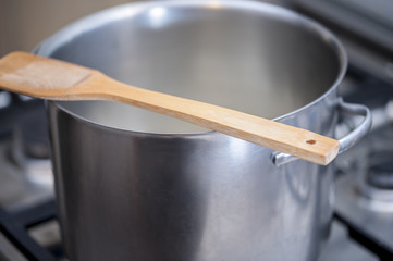 Wooden spoon over a hot metal pot while cooking a meal on a gas stove. Selective focus.